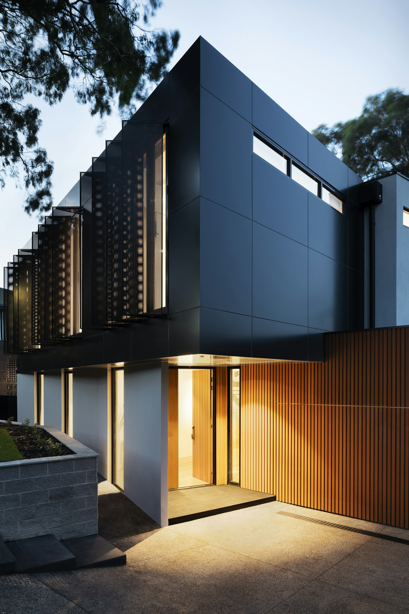 Modern home exterior with warm wood cladding and a lit entry